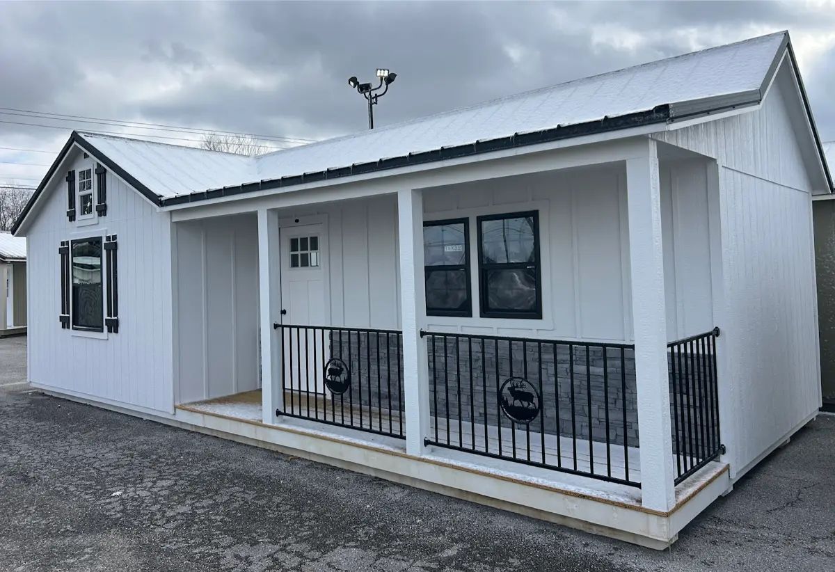 White tiny house with a front porch, black railing, and a metal roof.