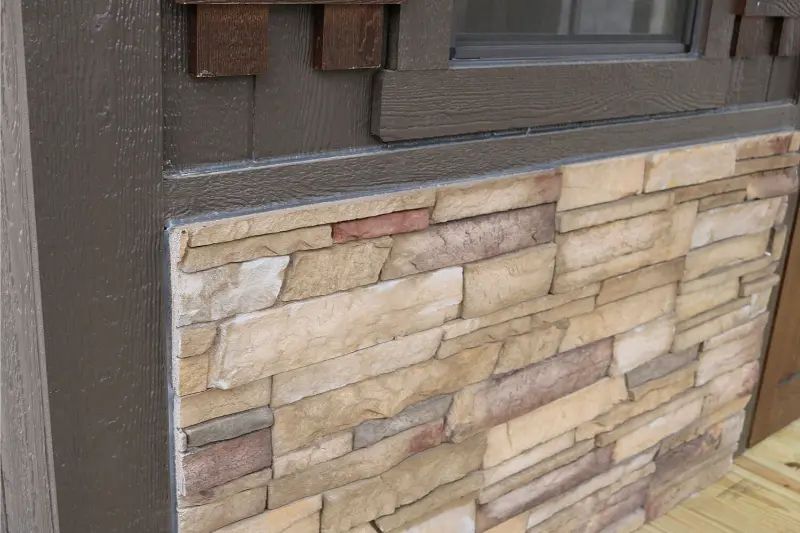 Stone veneer siding on a building, with dark brown trim and wooden accents near a window.