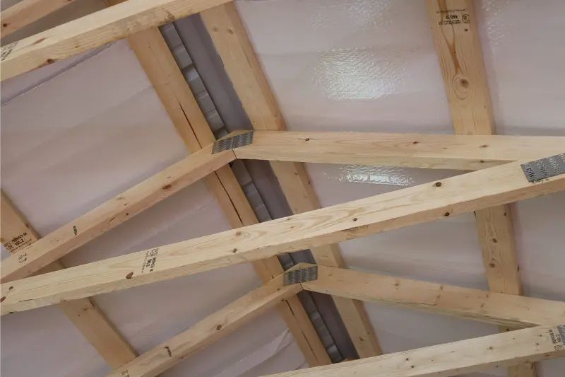 Wooden roof trusses with metal connectors, under white tarp.