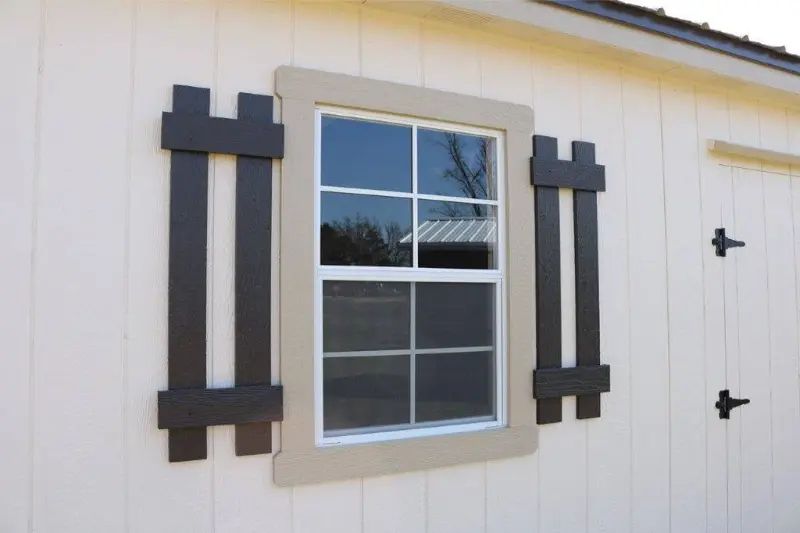 Window with dark brown decorative shutters on a beige building.