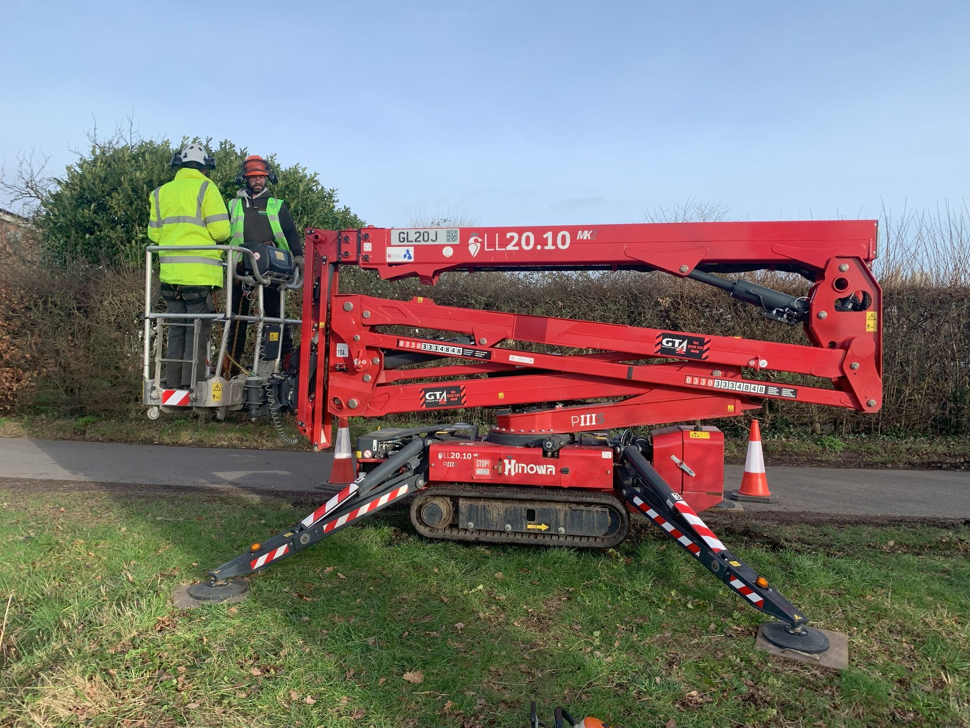 Two men are working on a red crane on the side of a road.