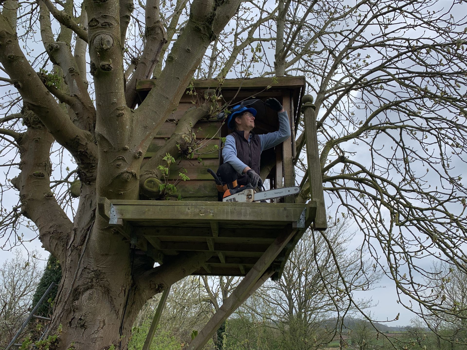 A man is sitting in a tree house with a chainsaw.