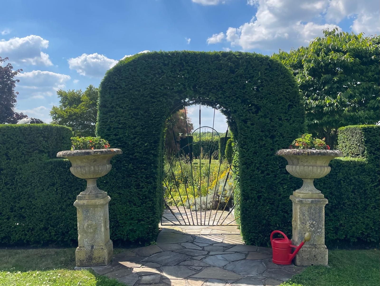 A red watering can sits in front of a garden gate