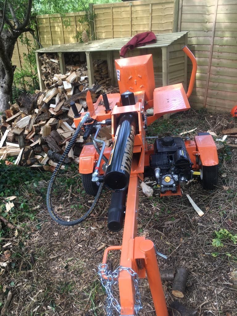 A wood splitter is sitting in the dirt next to a pile of wood.