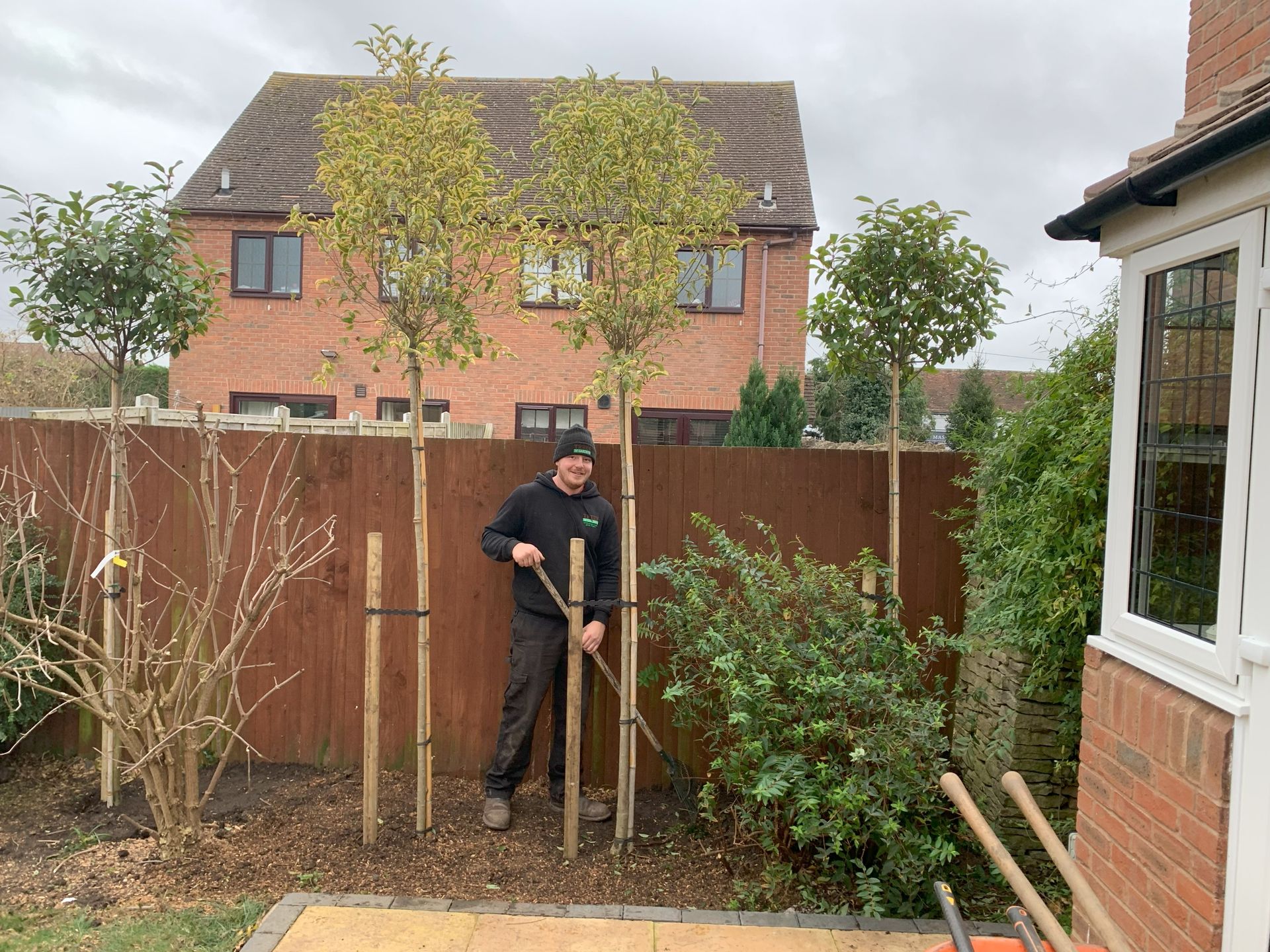 A man is standing in front of a wooden fence in a garden.