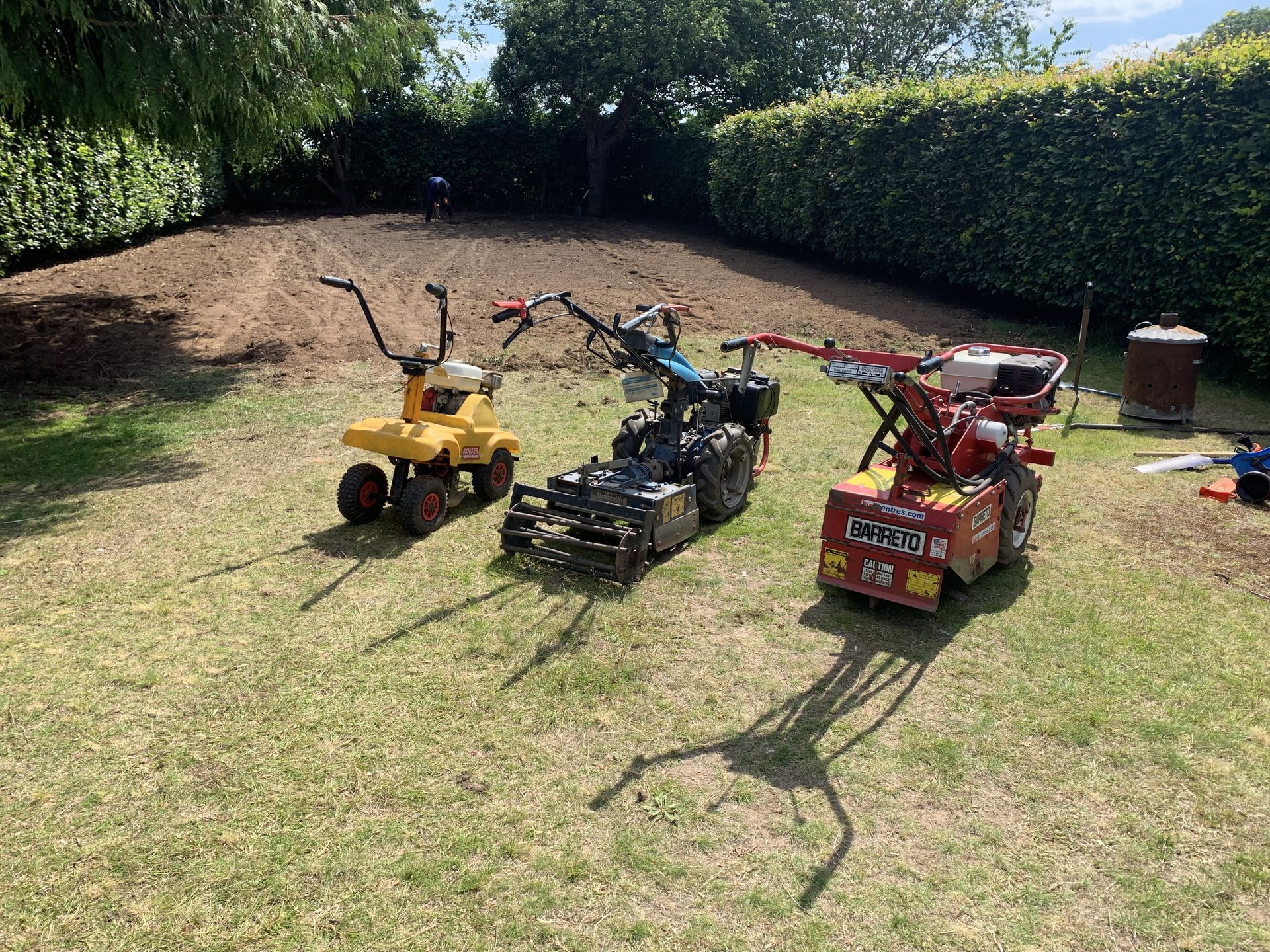 Three small tractors are parked in a grassy yard.