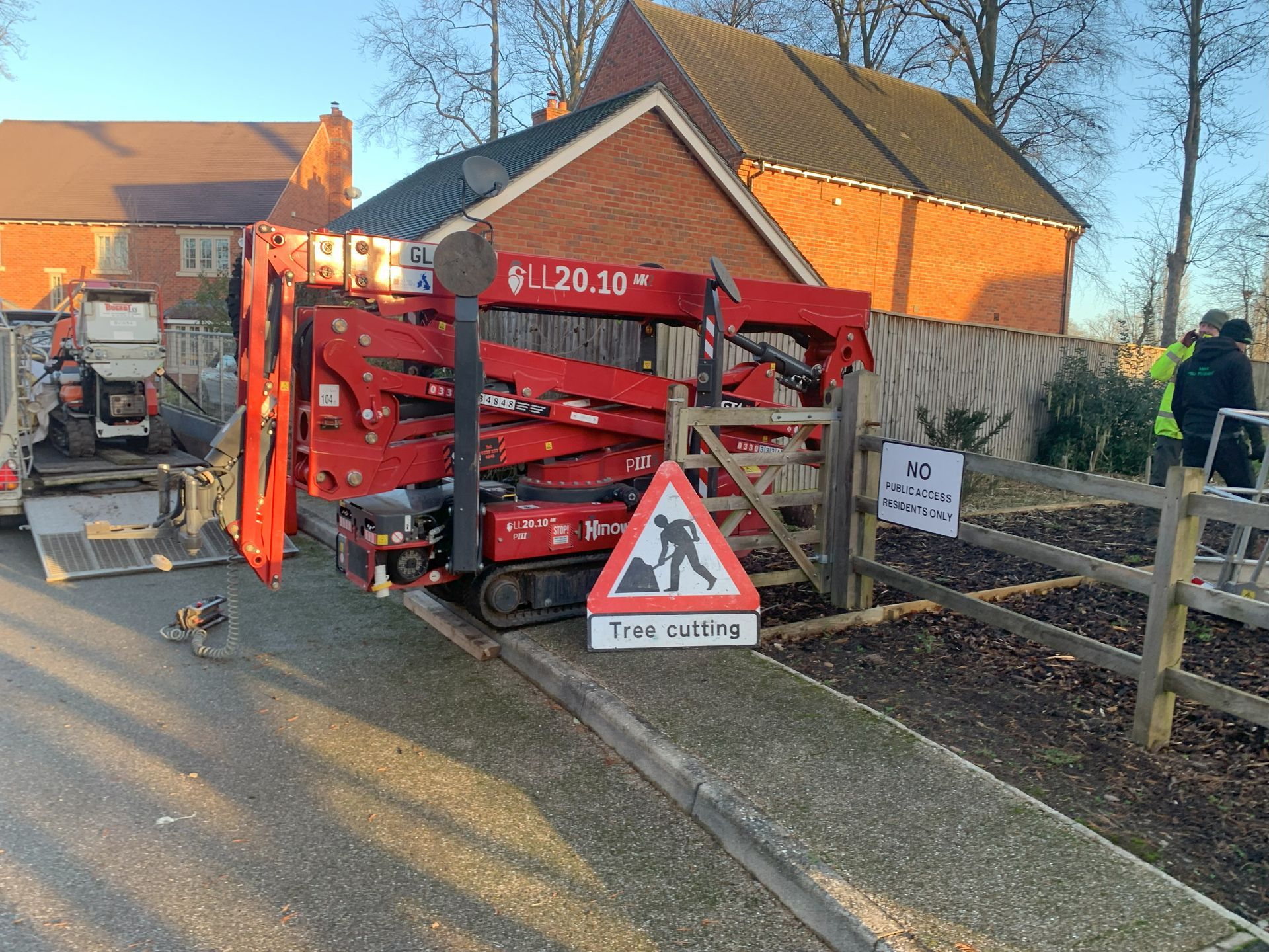 A red crane is parked on the side of the road next to a wooden fence.