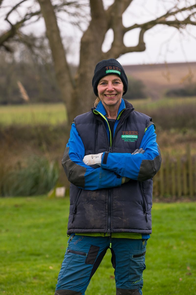 A man in a blue vest and black hat is standing in a field with his arms crossed.
