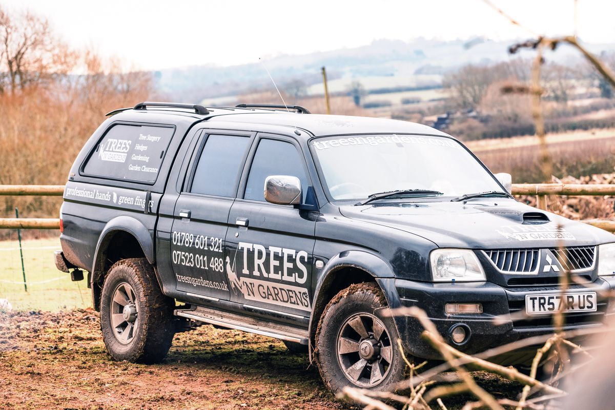 A black truck with the word trees on the side is parked in a field.