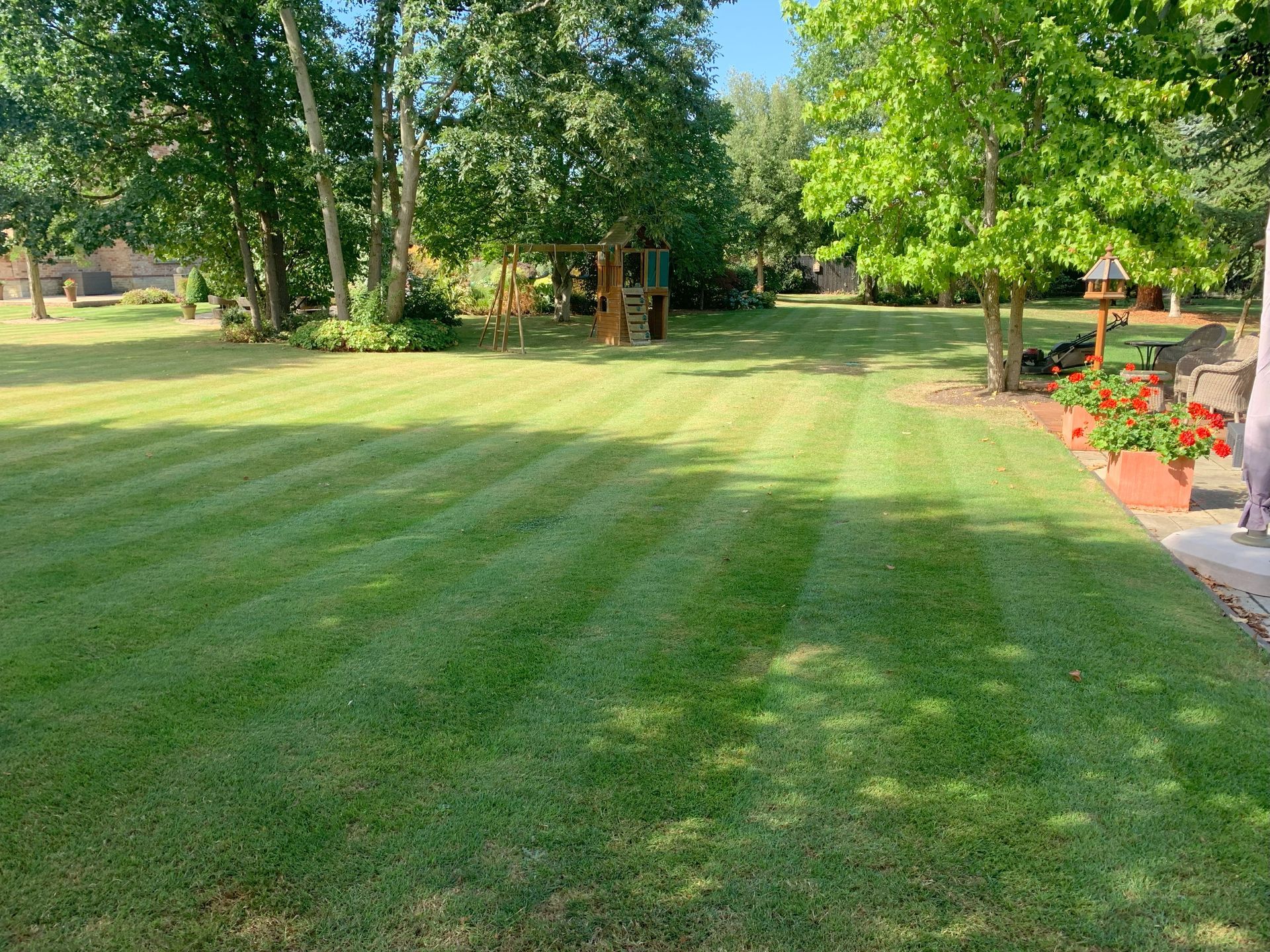 A lush green lawn with trees in the background and a playground in the background.