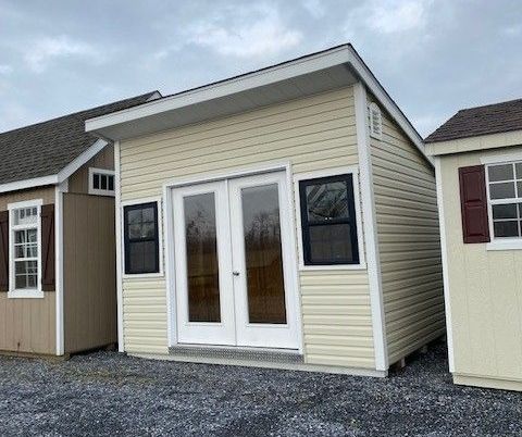 Lean-To shed with beige vinyl siding, white trim, 2 windows, and a set of double doors with windows.