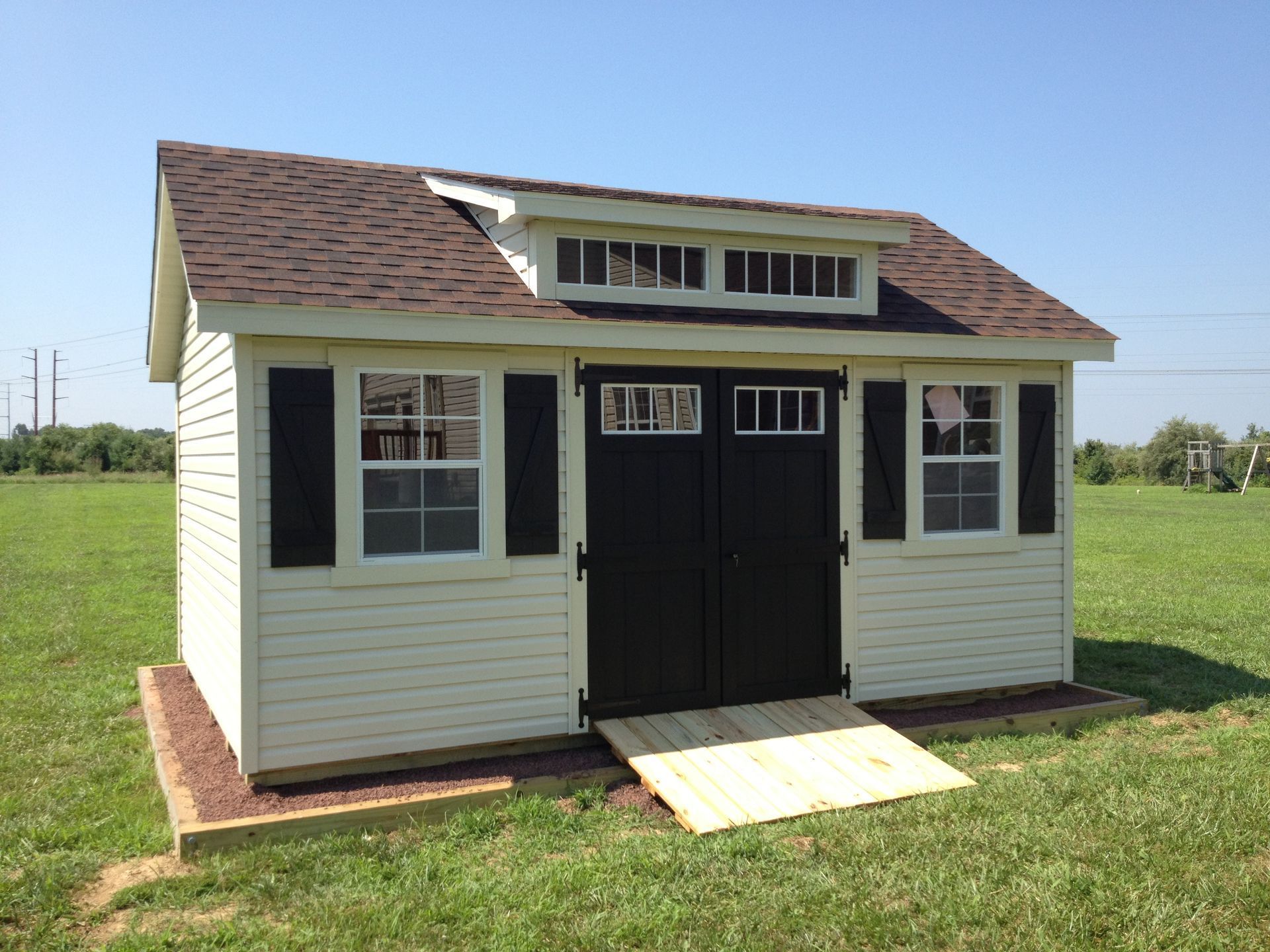 dormer shed with white siding, black doors and shutters, and ramp