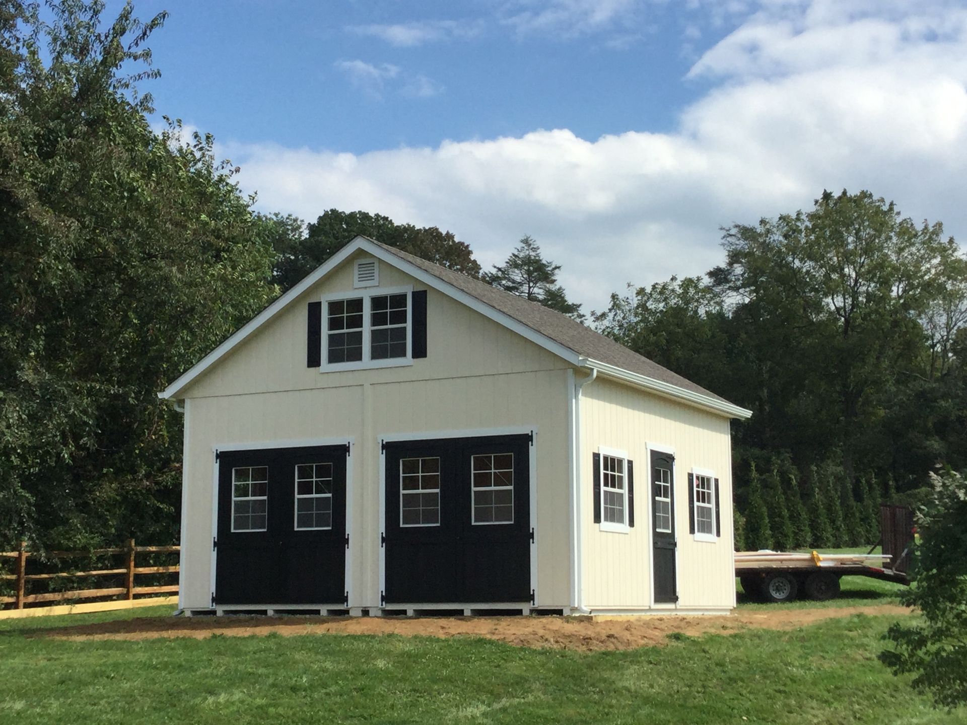 2 story doublewide garage with cream siding and 2 black garage doors
