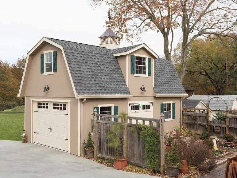 2 story Dutch Barn Shed with tan wood siding, white trim, windows with green shutters, white double doors, a white garage door, and gray asphalt roofing.