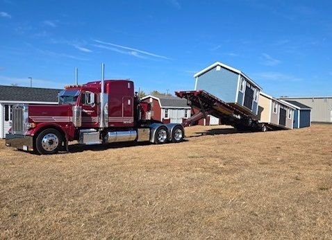 red truck hauling two blue and one white shed to a new location from the shed lot