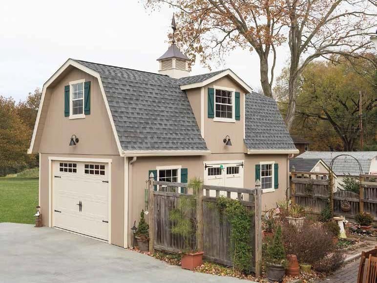 2 story dutch barn garage with tan siding, white doors, and green shutters