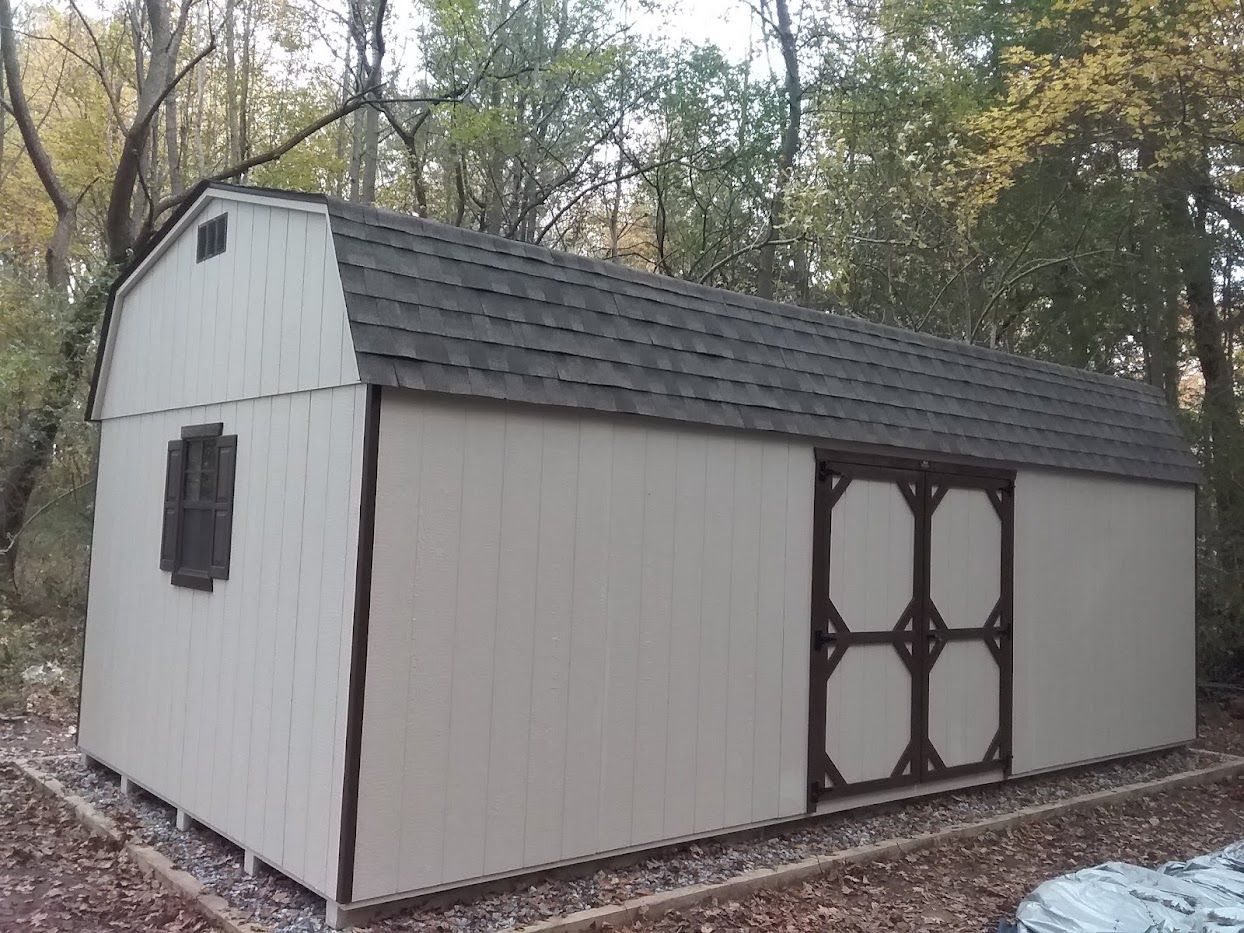 Light-colored shed with dark trim, a black window with dark shutters, a set of double doors, and a gray asphalt roof.