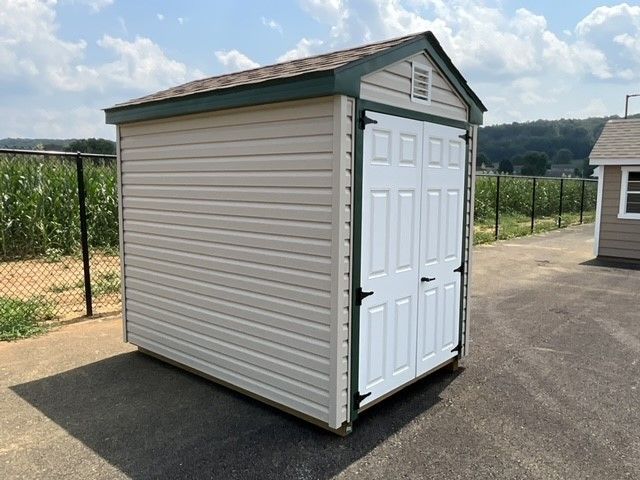 Light-colored vinyl shed with dark trim, asphalt roofing, and white double doors.