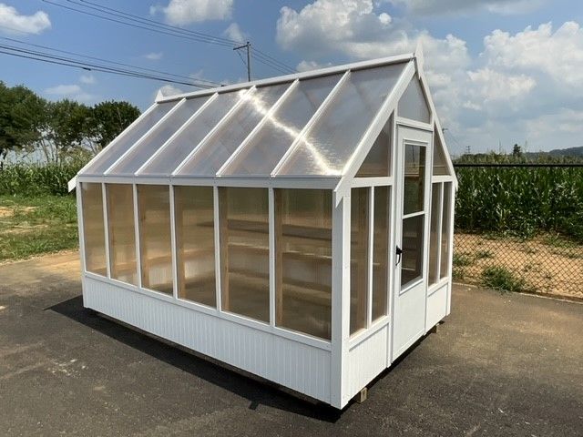 White green house with clear sides, a clear roof, and a single entry door.