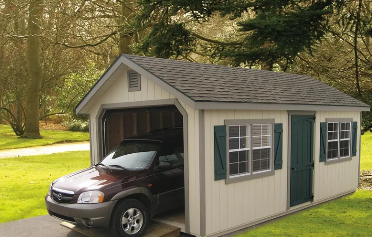 tan detached garage with green doors and window shutters with a red car inside