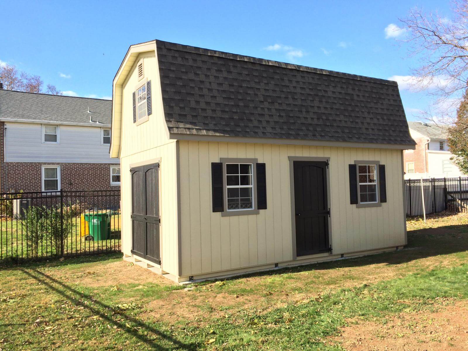 Beige two-story single-car garage with windows and black shutters, black doors, and a black roof