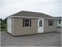 Hip Roof shed with tan vinyl siding, a set of white double doors, a white single-entry side door with windows, 2 white windows with dark red shutters, and a brown asphalt roof.