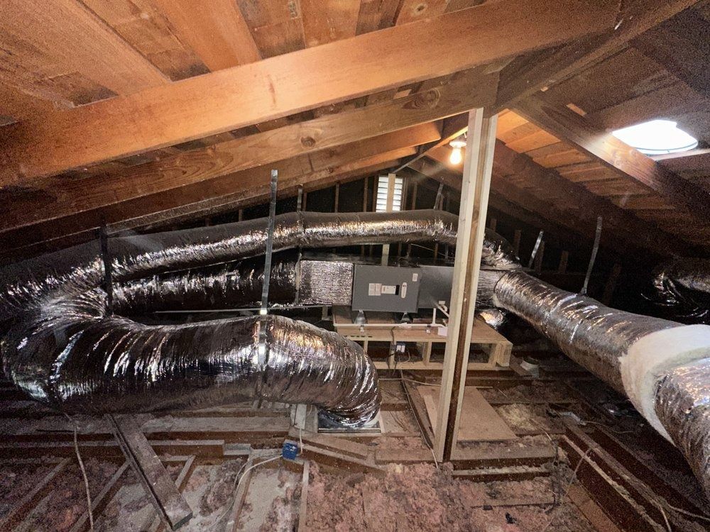 Attic with wooden beams, insulation, and HVAC ductwork snaking through the space.