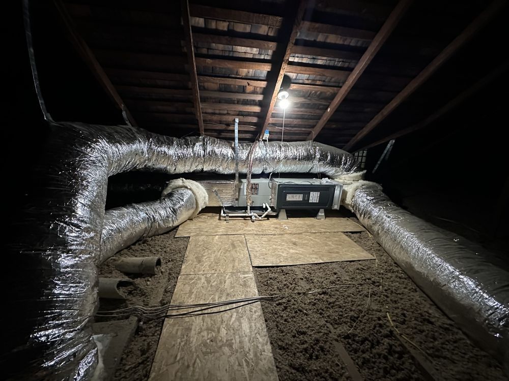 HVAC system in an attic with ductwork. Insulation and wooden beams are visible.
