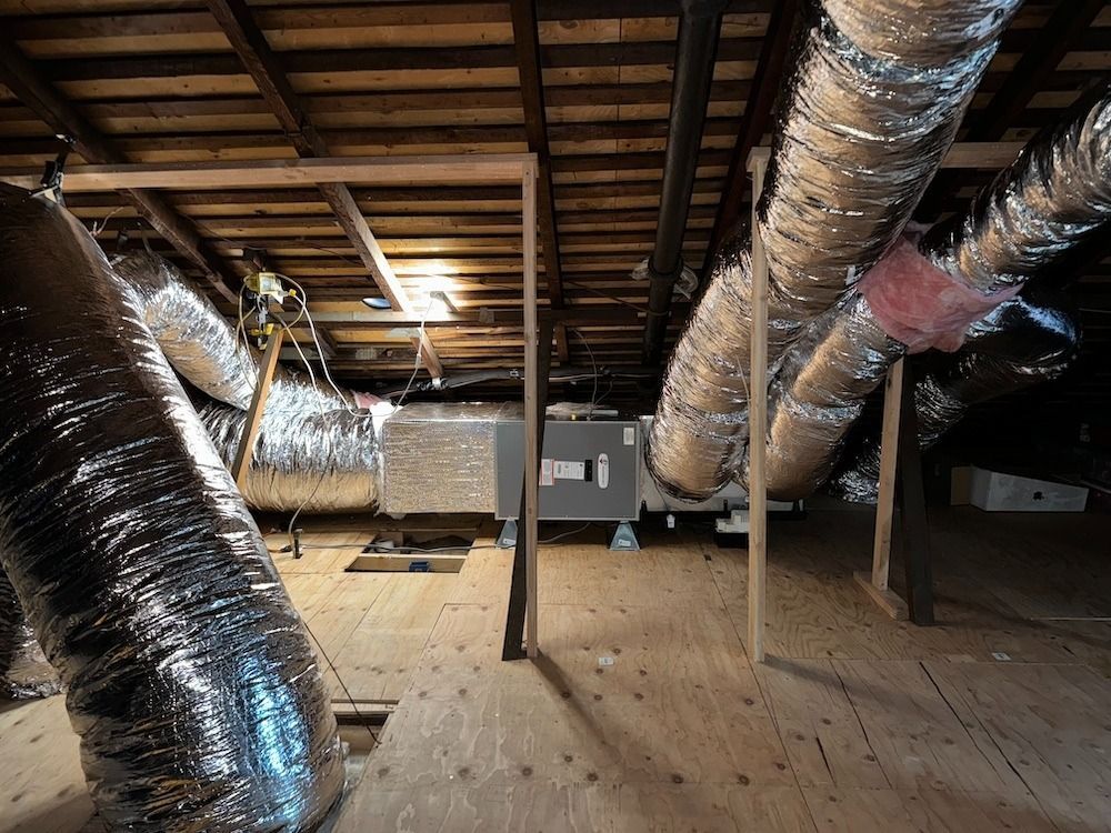 An attic with HVAC ductwork, wood framing, and insulation.