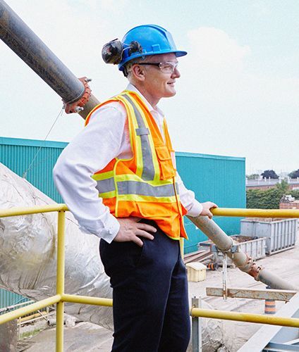 Man in hard hat and safety vest, surveying industrial site from a platform.