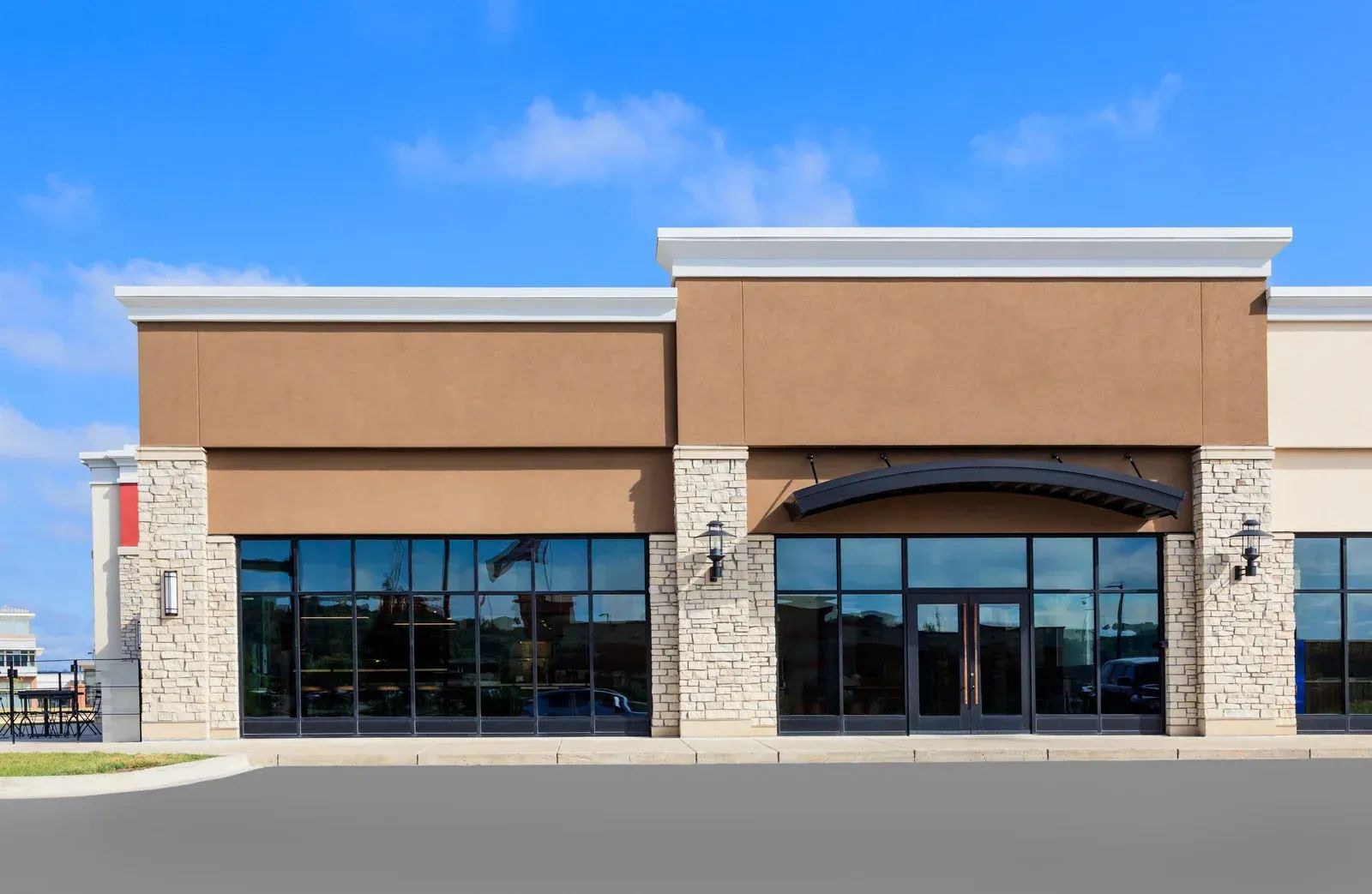A modern, tan-colored storefront with stone accents and large glass windows under a clear blue sky.
