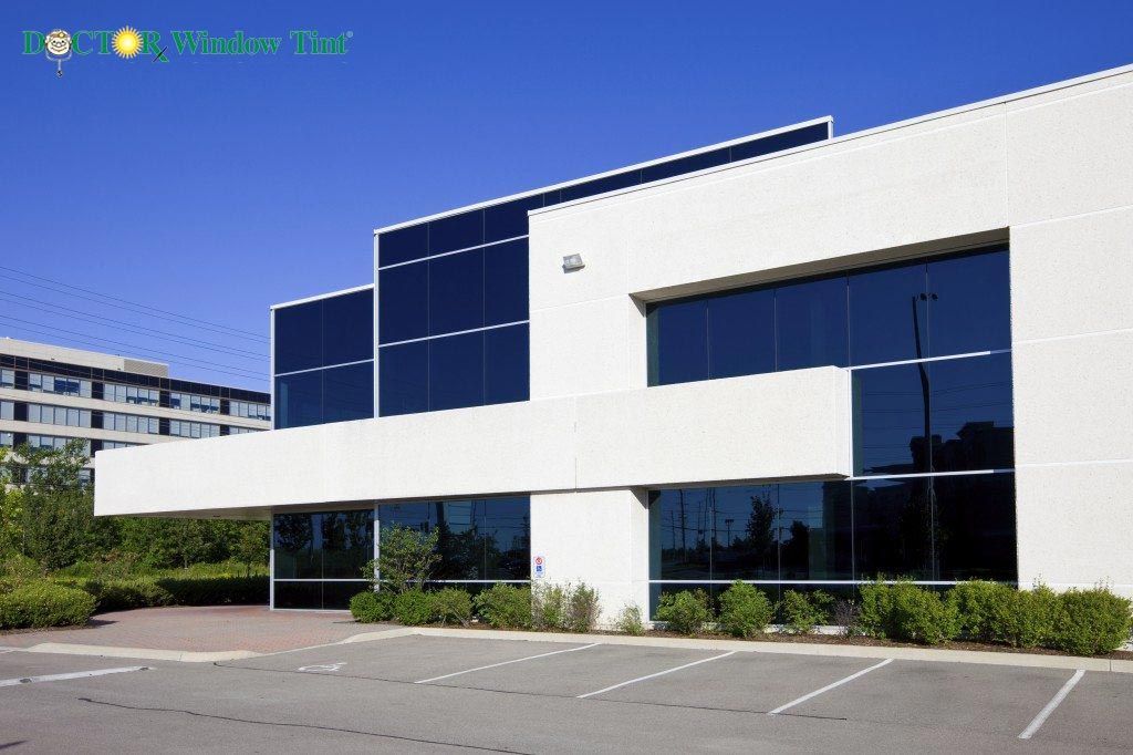 Modern white office building with large tinted windows under a bright blue sky.