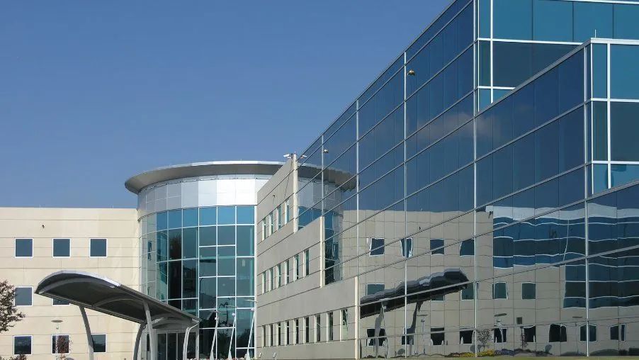Modern office building with reflective blue glass and a cylindrical glass and metal entryway.