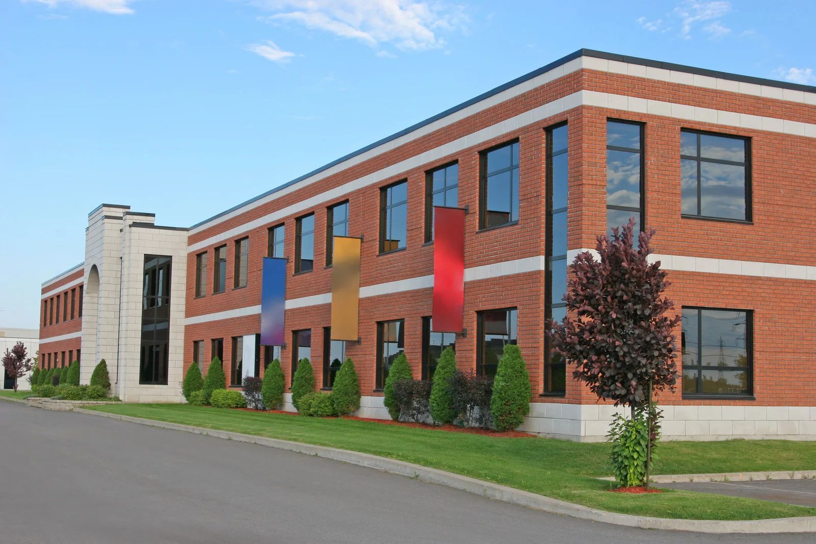 Red brick office building with colorful banners, green lawn, and blue sky.