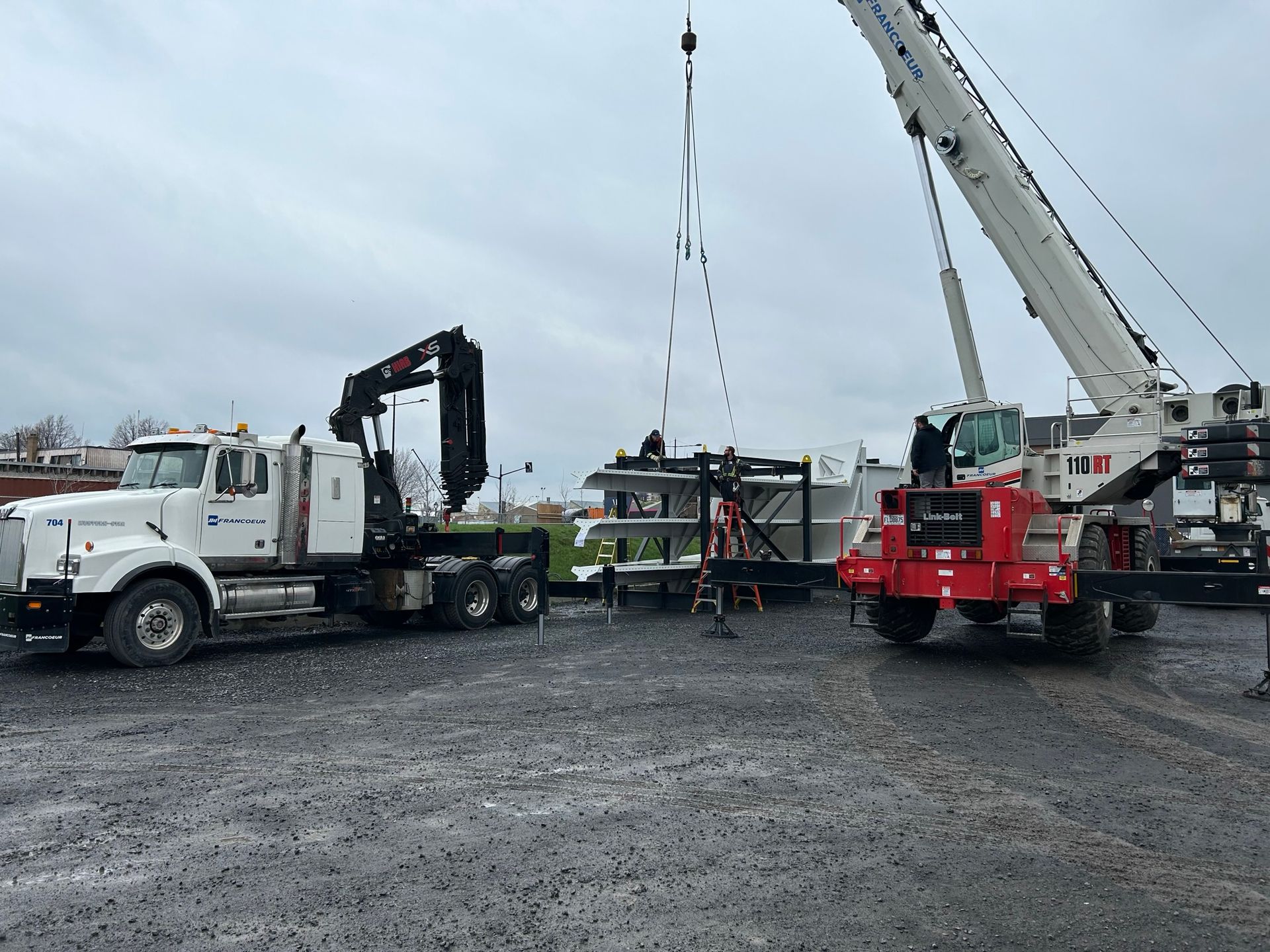 Un camion avec une grue attachée est garé sur un terrain en gravier.