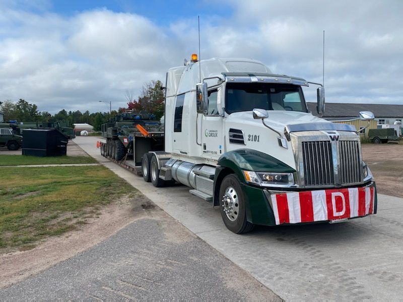 Un semi-camion transporte un véhicule militaire sur une remorque.