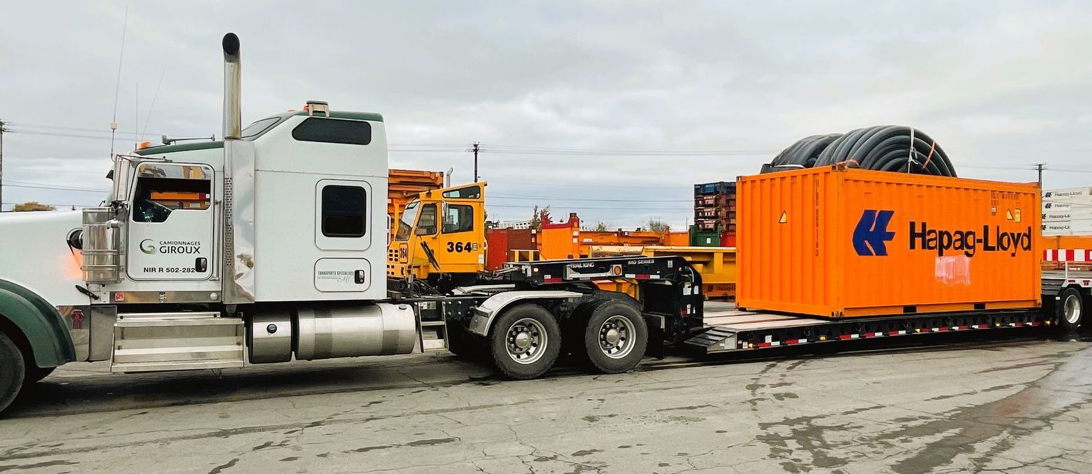 Un semi-remorque tire un grand conteneur orange sur une remorque.