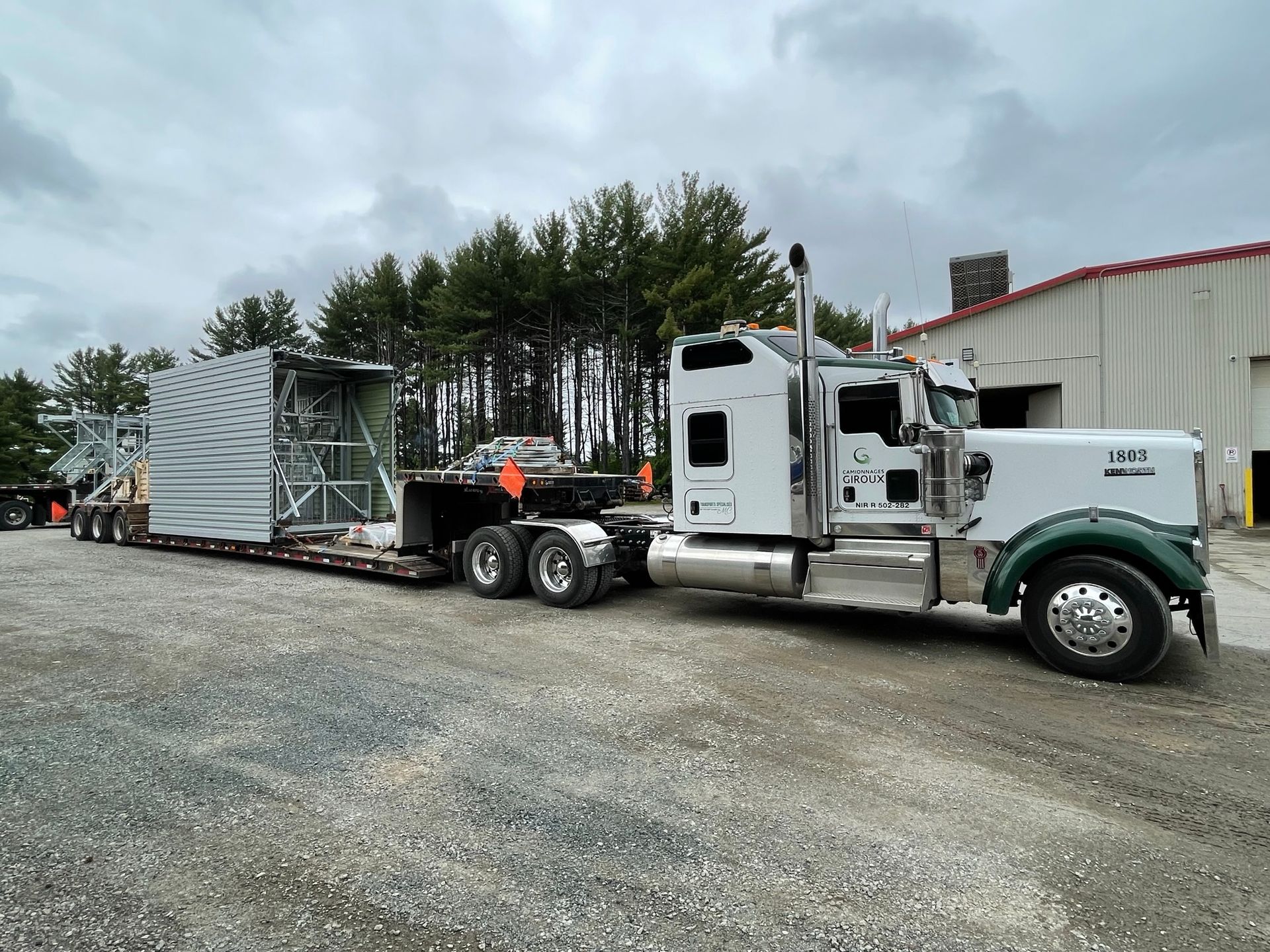 A semi truck with a trailer attached to it is parked in a gravel lot.