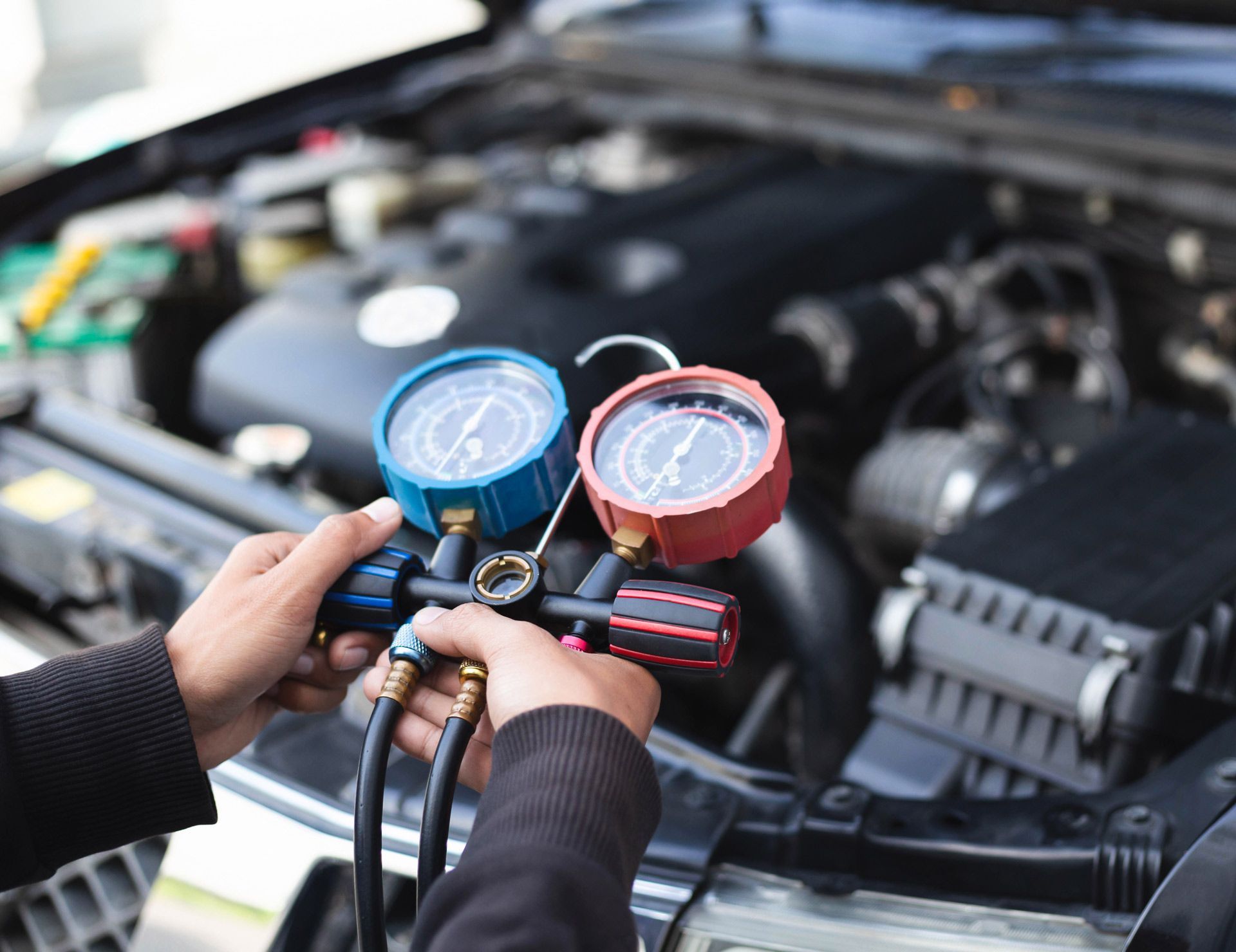 Hands connecting gauges to car engine for AC check.