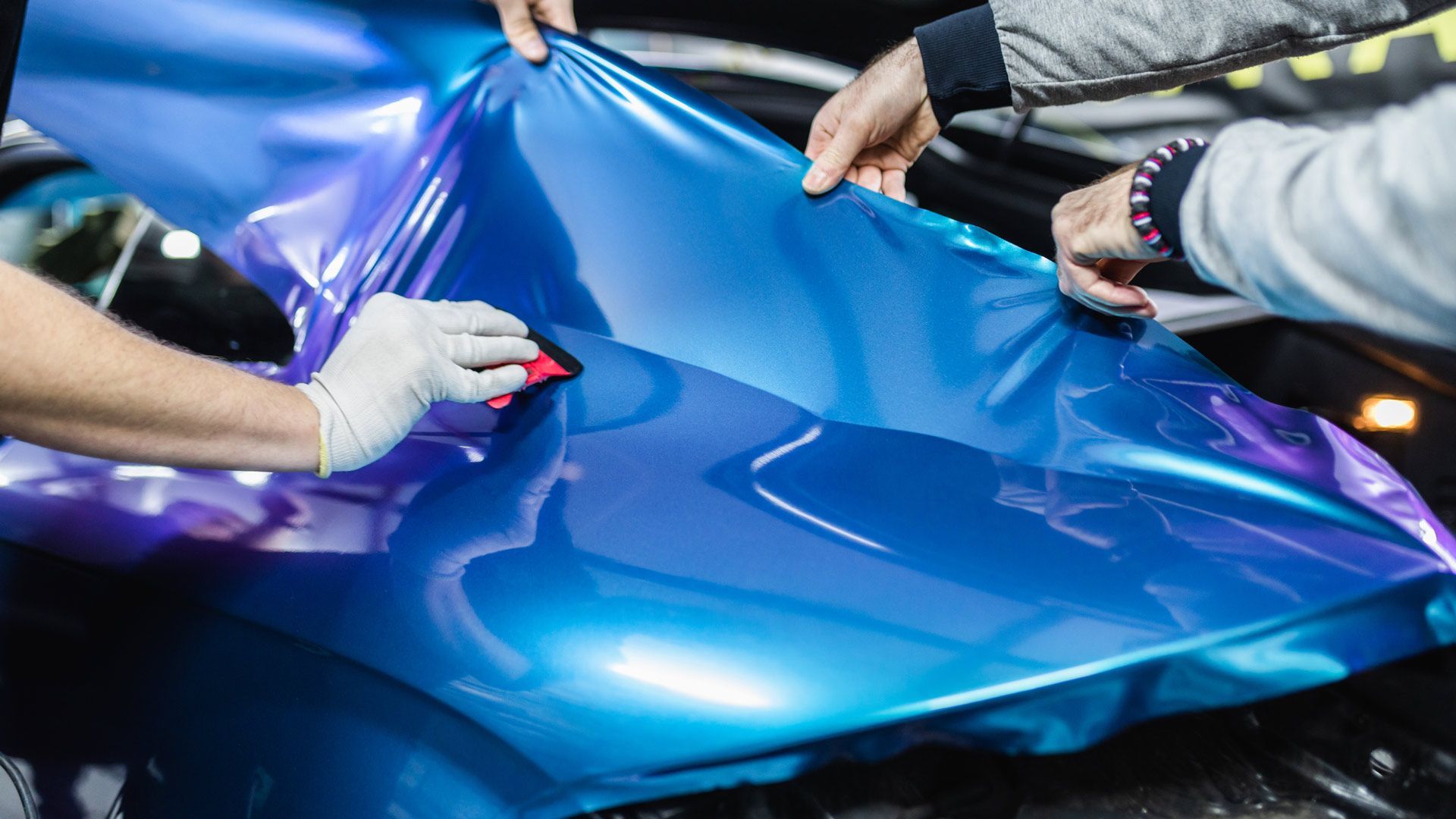 Hands applying blue car wrap to a vehicle's body.