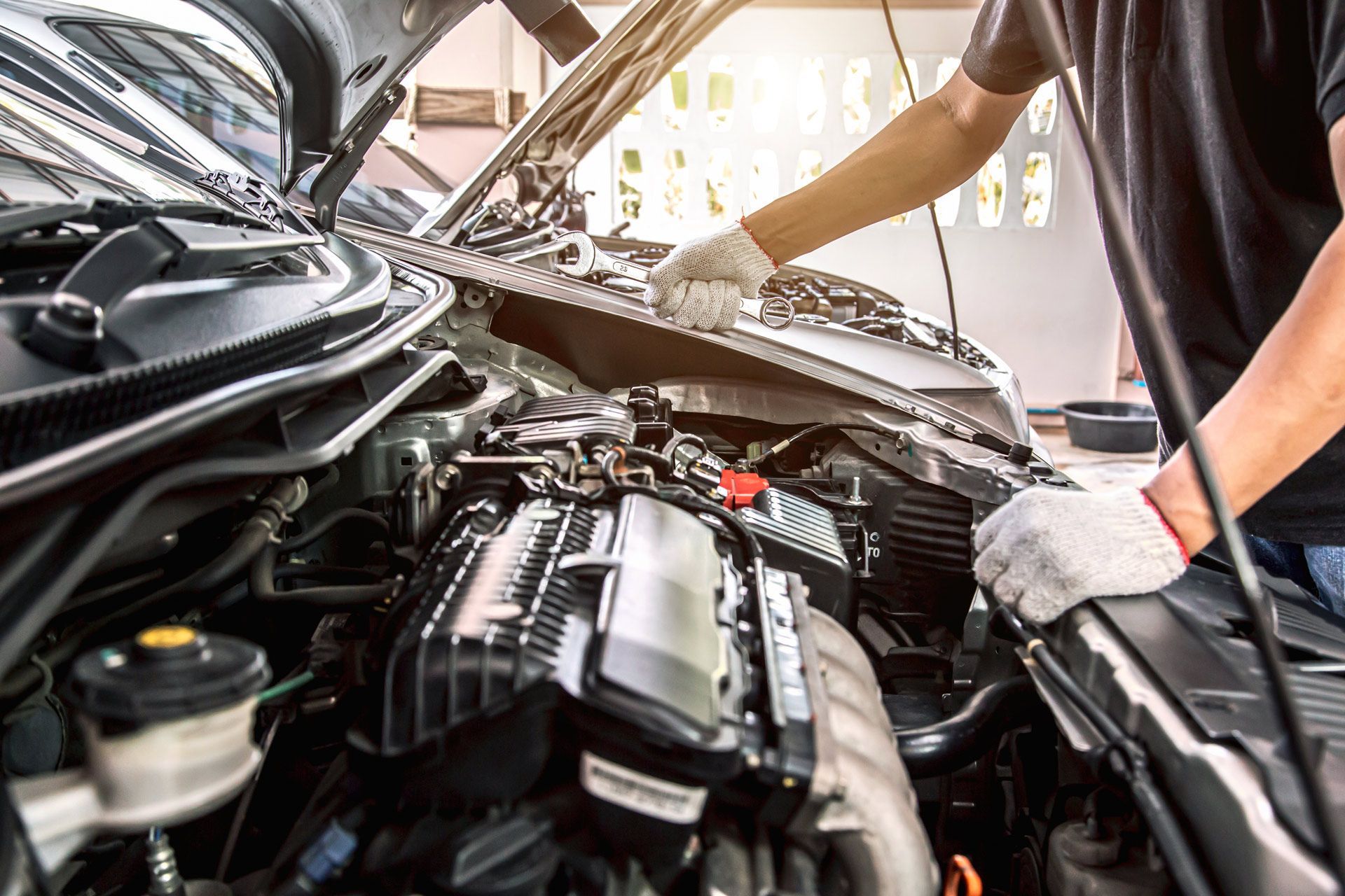 Mechanic working on car engine, wearing gloves, in a garage.