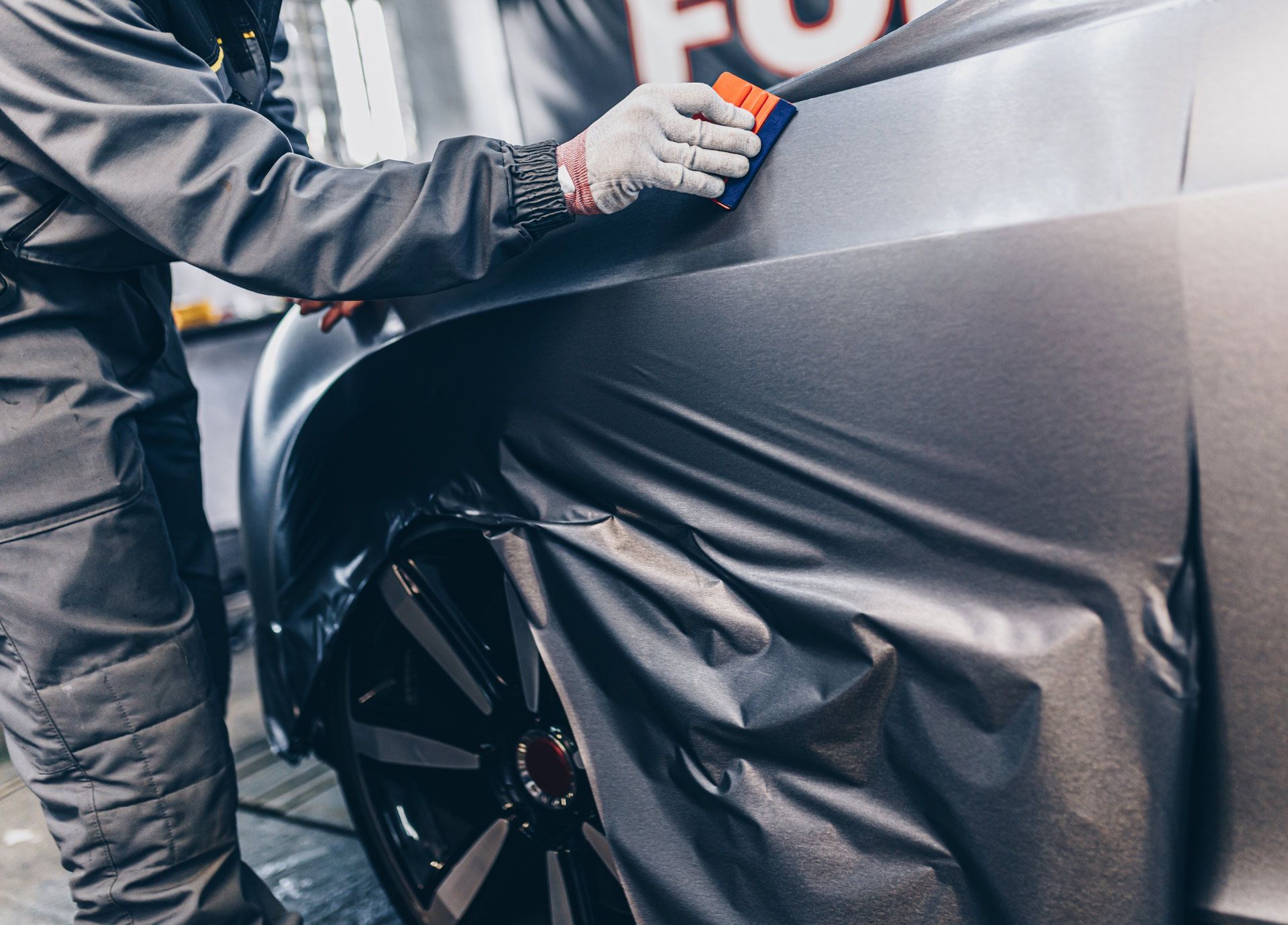 Person applying gray vinyl wrap to a car's rear quarter panel with a squeegee.