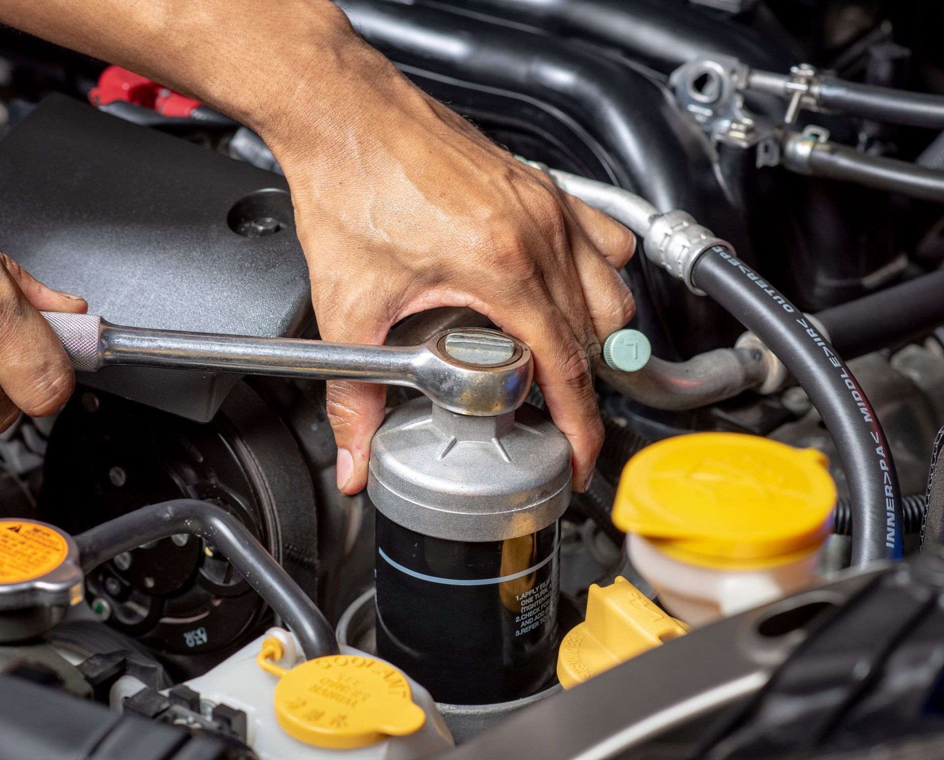 Hands using a wrench to remove an oil filter from a car engine.