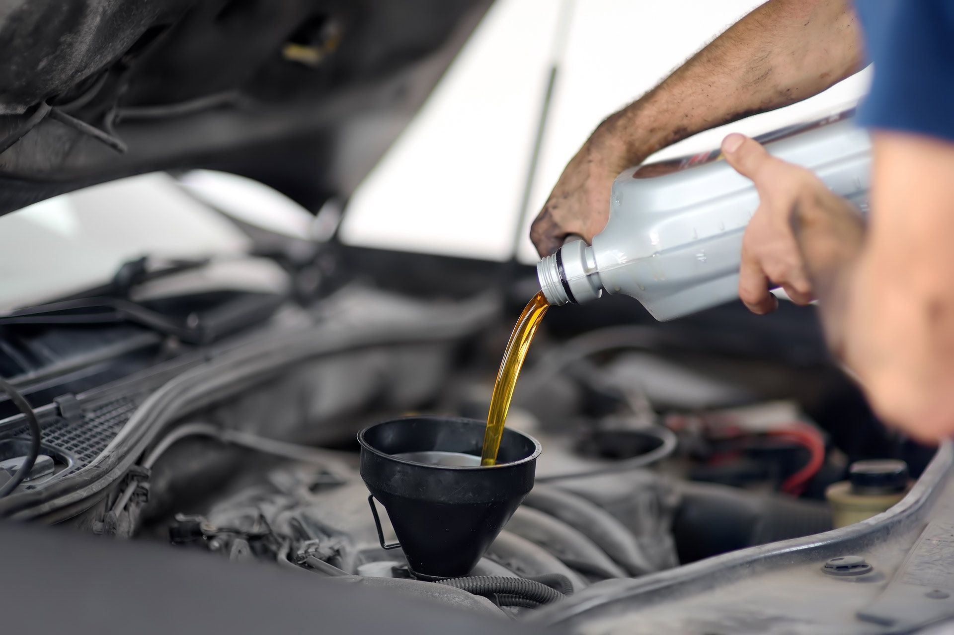 Person pouring oil into a car engine with a funnel.