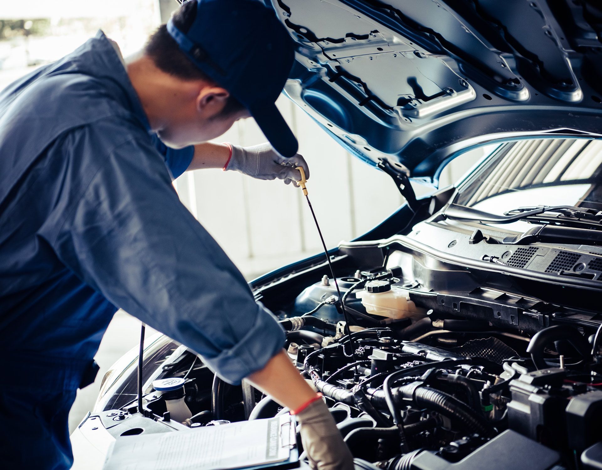 Mechanic checking car engine oil with a dipstick in a garage.