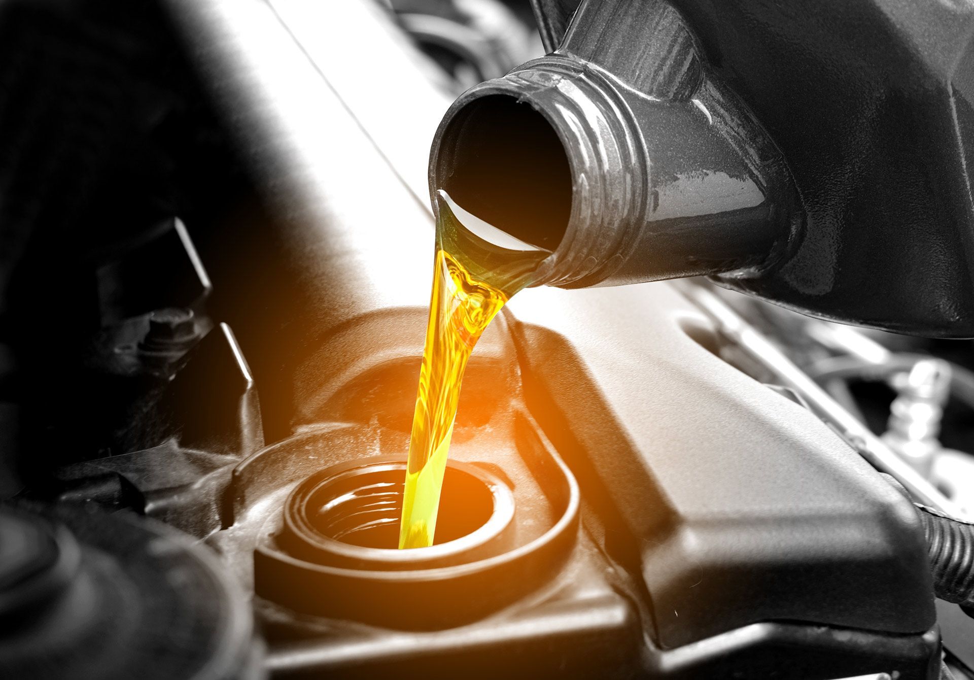 Yellow oil pouring from a container into a car engine.