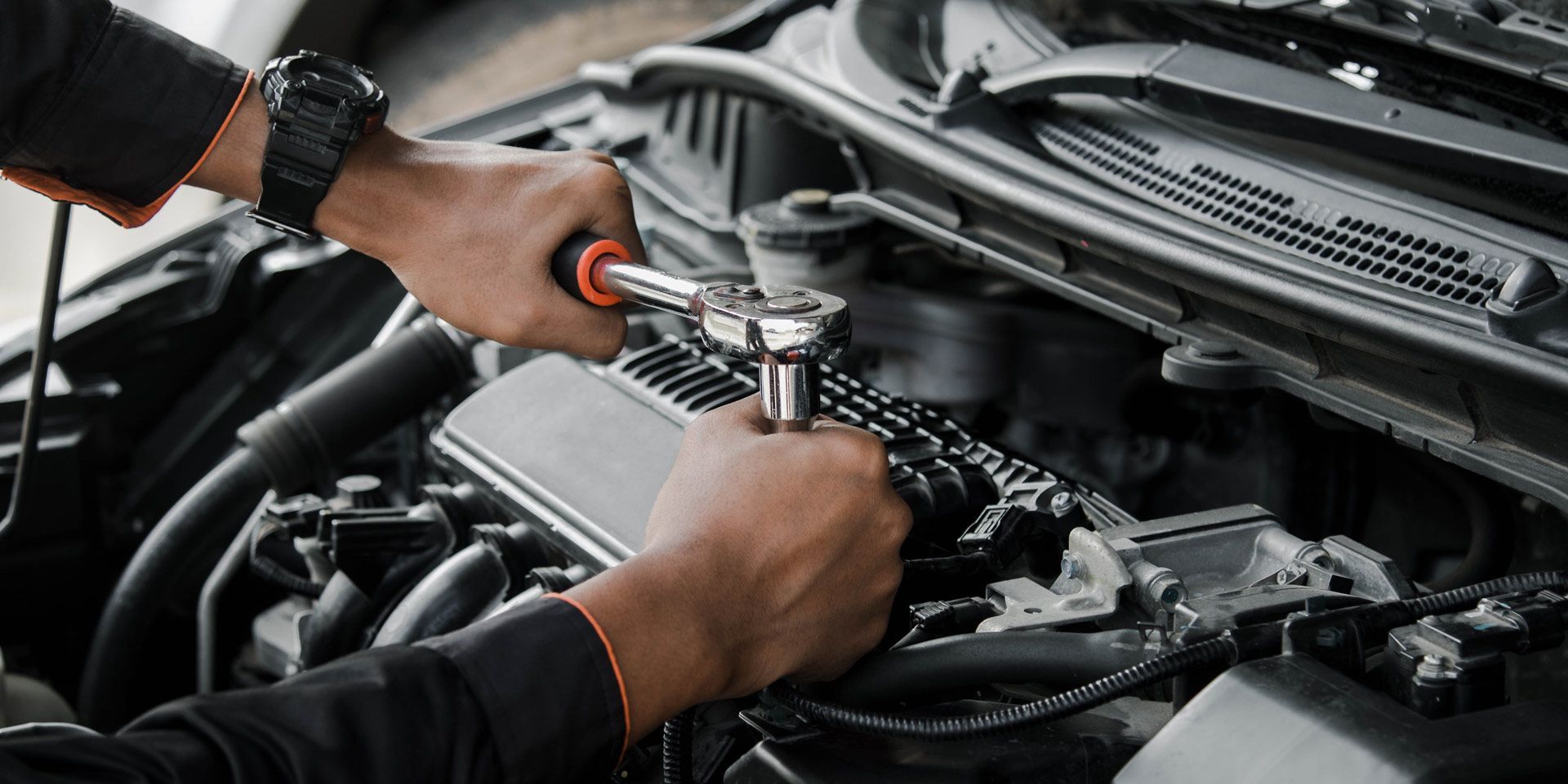 A mechanic uses a ratchet to work on a car engine, under the hood, close up shot.