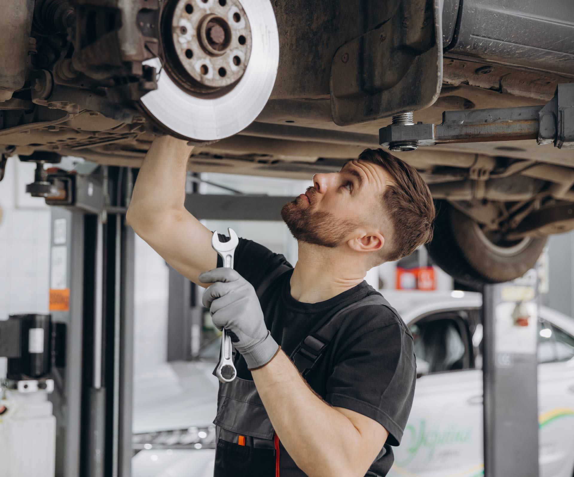 Mechanic working on a car brake, holding a wrench, under vehicle, in a garage.