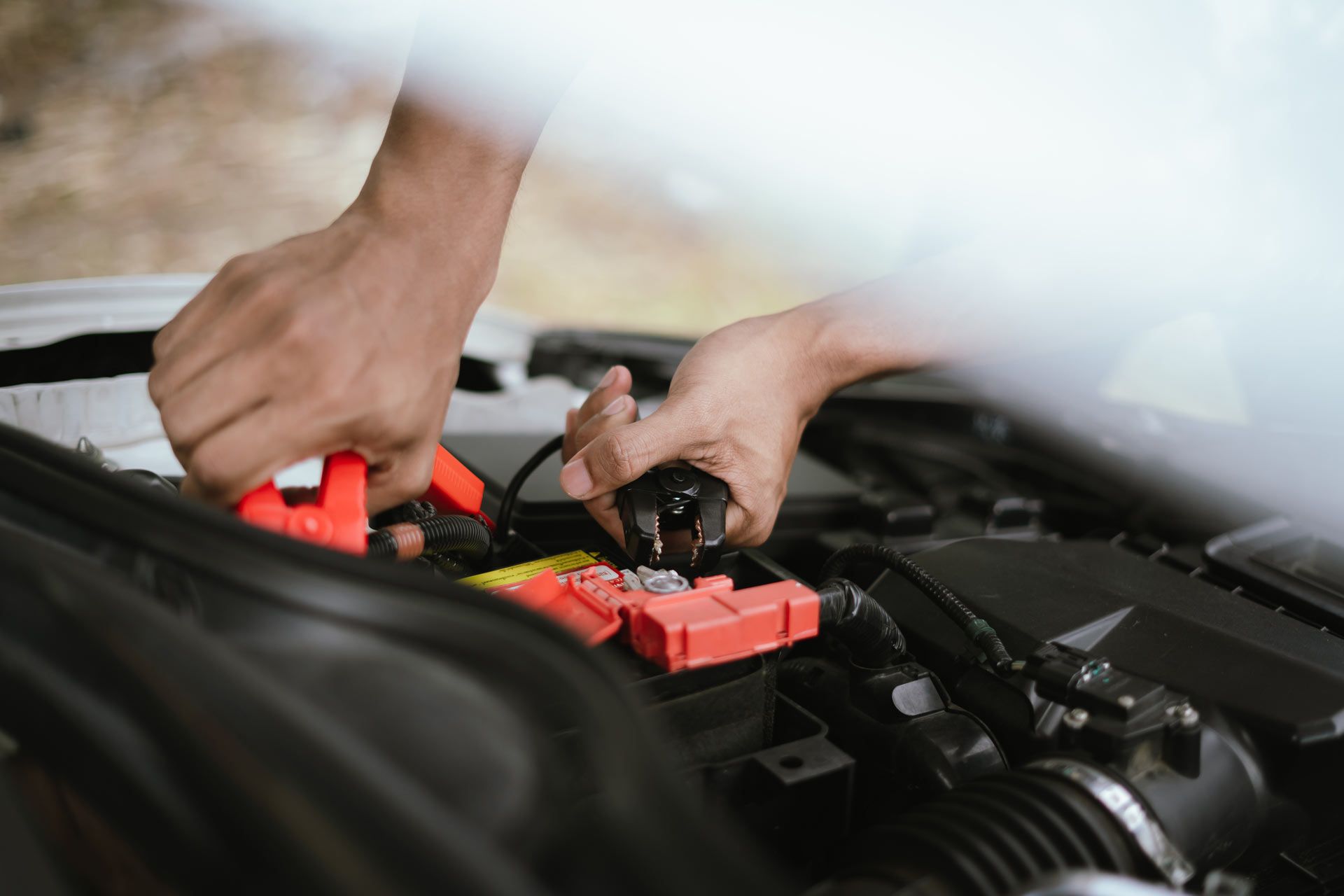 Hands connecting jumper cables to a car battery.