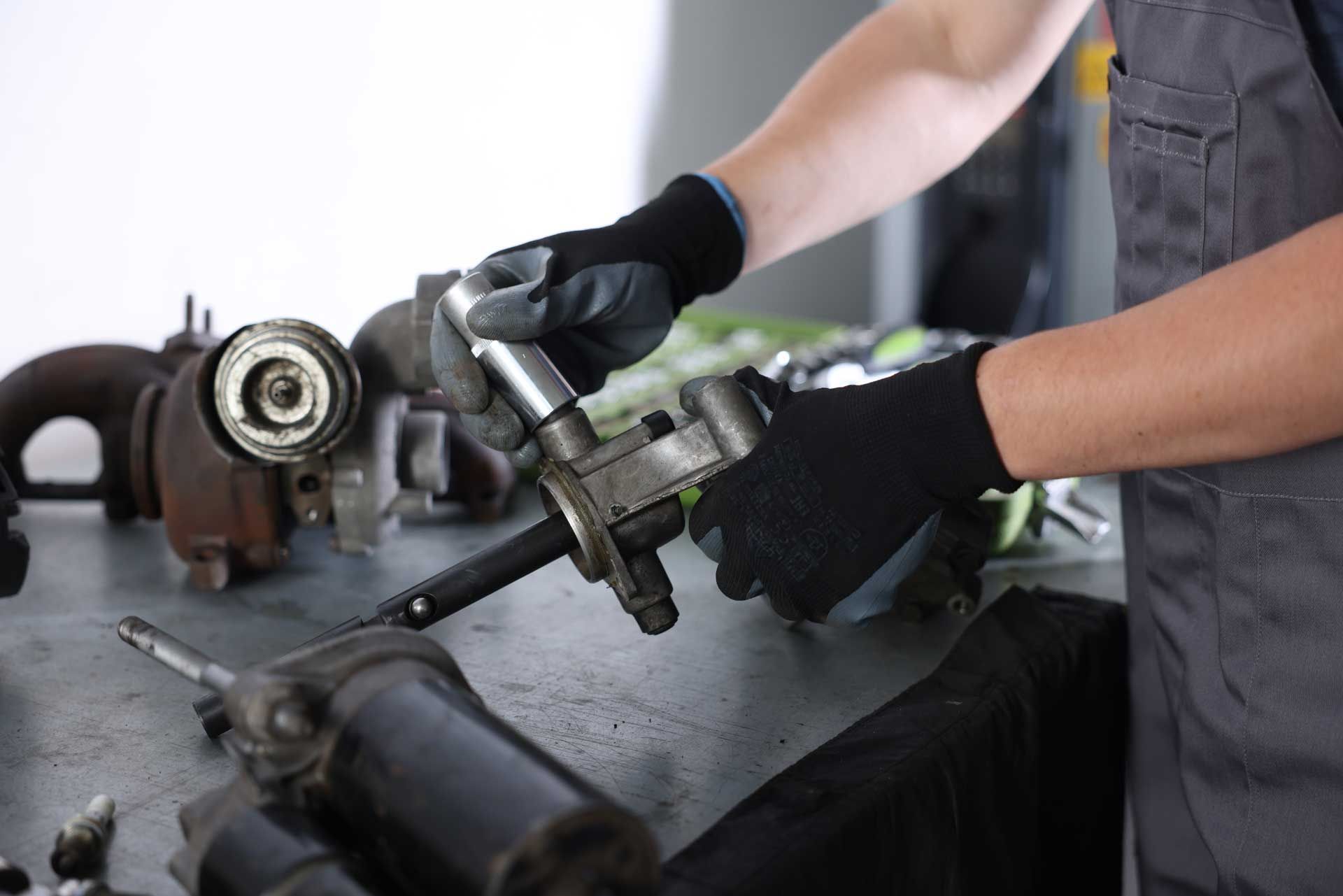Mechanic in gloves working on car parts on a workbench.